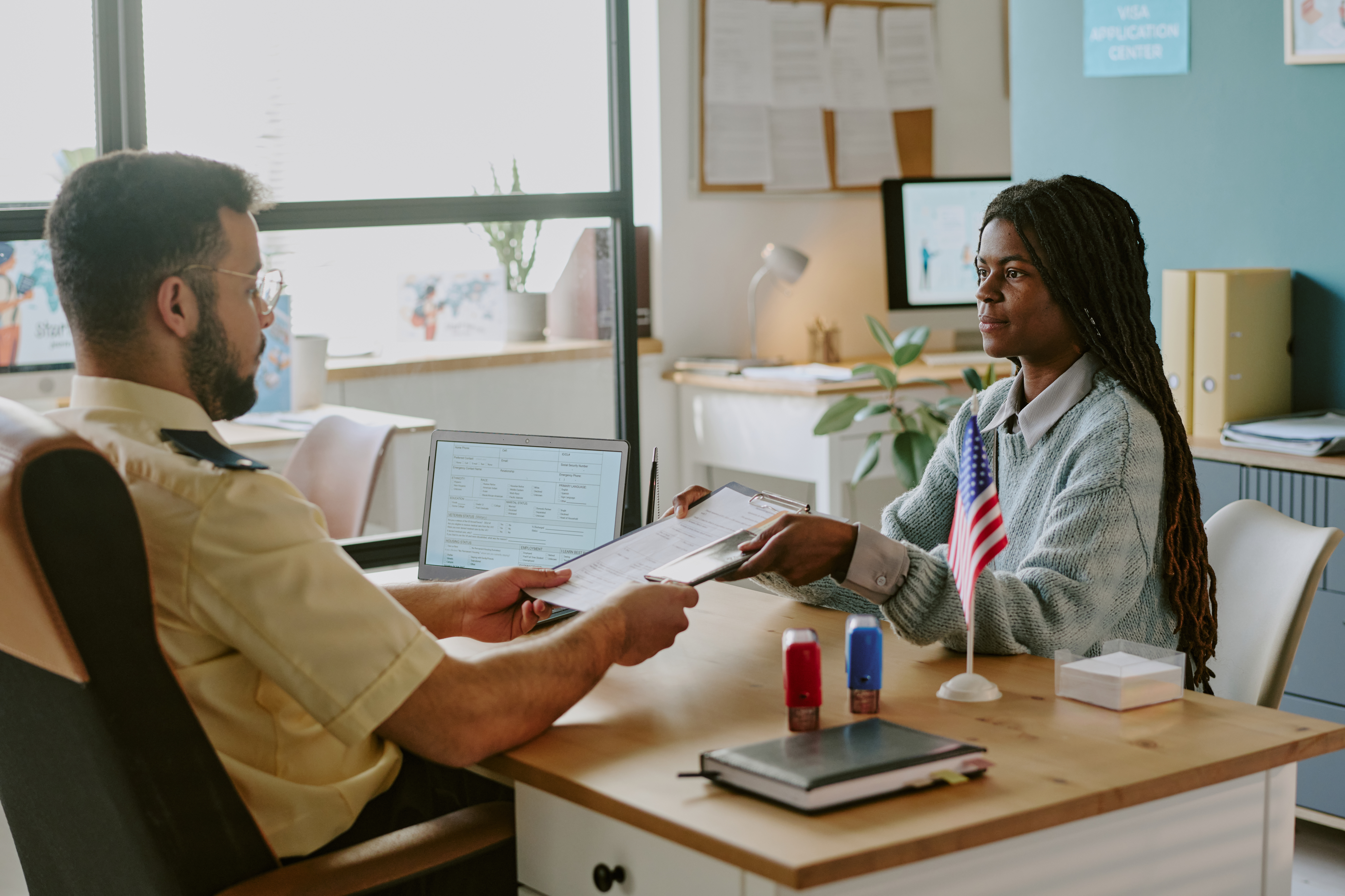 Officer Handing Documents to Woman in Office Setting Young woman hands immigration officer paper work over desk in office