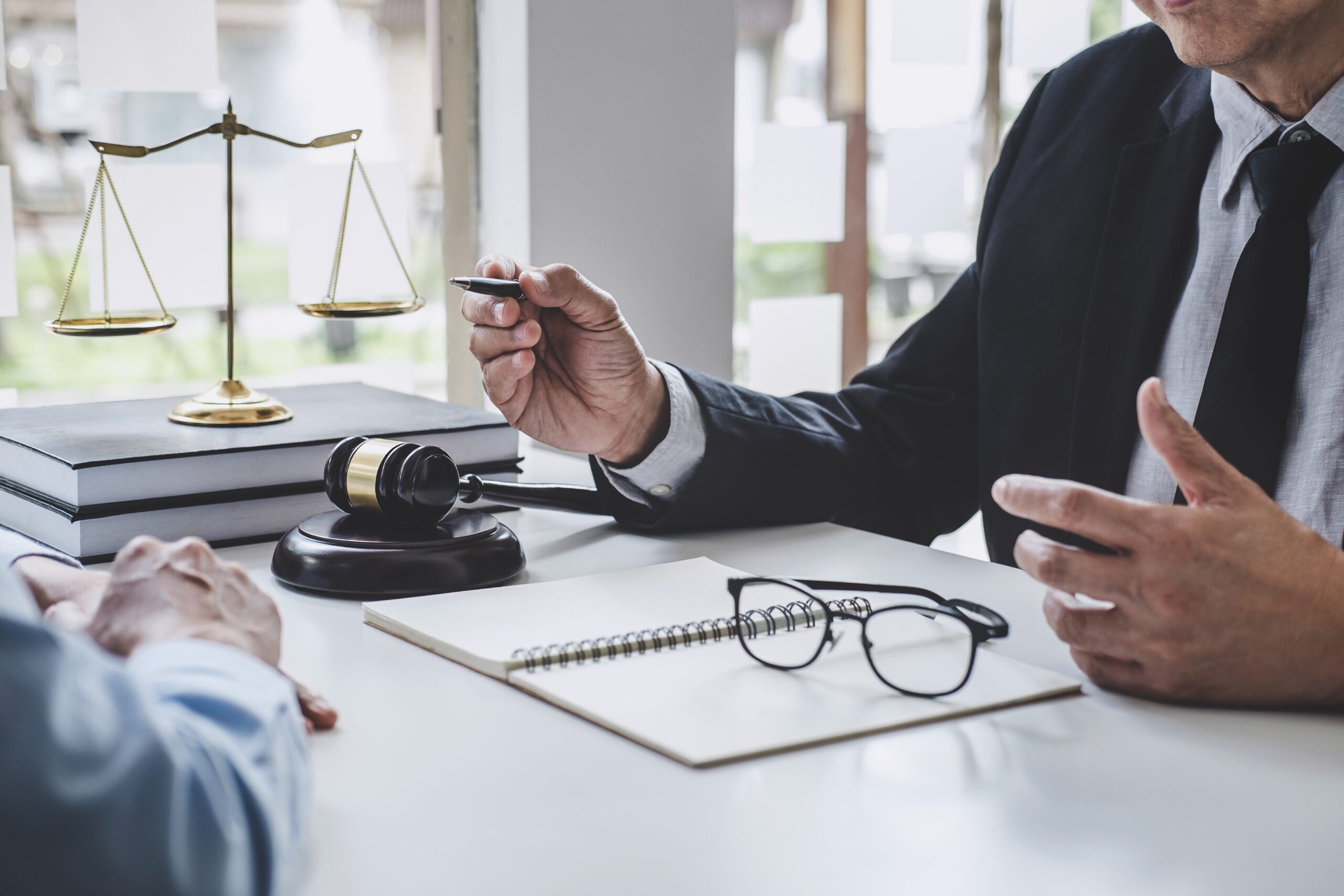 a lawyer sitting at a desk with a client and a notepad and gavel and scale at his desk